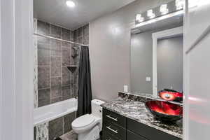 Full bathroom featuring vanity, shower / bath combo with shower curtain, a textured ceiling, and toilet