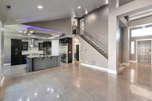 Kitchen with wall chimney range hood, an island with sink, a high ceiling, and built in refrigerator