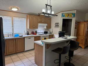 Kitchen with a textured ceiling, pendant lighting, white appliances, and light tile patterned floors