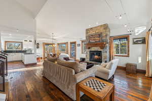 Living room featuring a notable chandelier, a stone fireplace, wood-type flooring, and high vaulted ceiling