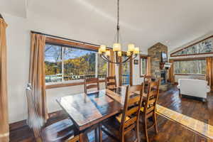 Dining room featuring a stone fireplace, vaulted ceiling, a wealth of natural light, and dark hardwood / wood-style floors