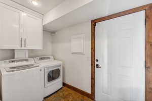 Clothes washing area featuring electric panel, cabinets, and washer and clothes dryer