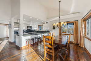 Dining space with a notable chandelier, high vaulted ceiling, sink, and dark hardwood / wood-style floors