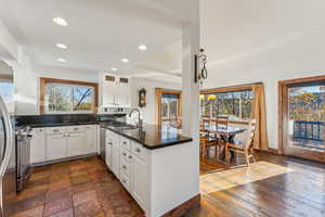 Kitchen with white cabinets, sink, dark stone counters, stainless steel stove, and dark wood-type flooring