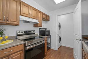 Kitchen featuring light hardwood / wood-style flooring, stainless steel electric range, and stacked washer and clothes dryer