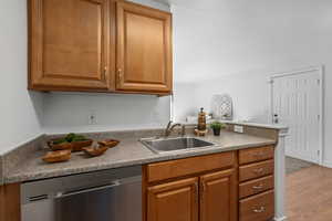 Kitchen featuring stainless steel dishwasher, sink, kitchen peninsula, and light wood-type flooring