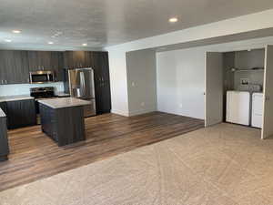 Kitchen featuring a kitchen island, washer and clothes dryer, dark brown cabinets, hardwood / wood-style floors, and appliances with stainless steel finishes