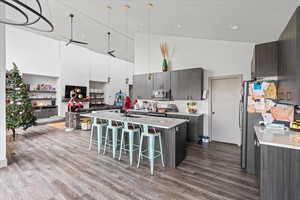 Kitchen with ceiling fan, stainless steel appliances, high vaulted ceiling, wood-type flooring, and a kitchen island with sink