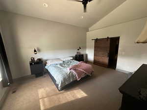 Bedroom with lofted ceiling, a barn door, carpet floors, and ceiling fan