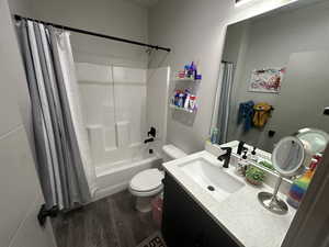 Full bathroom featuring hardwood / wood-style flooring, tile walls, toilet, shower / bath combo with shower curtain, and vanity