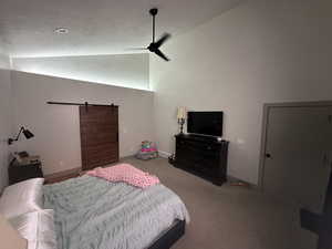 Carpeted bedroom featuring a barn door, vaulted ceiling, and ceiling fan