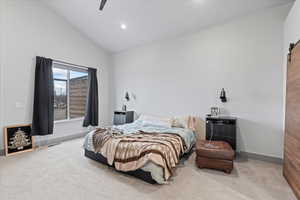 Bedroom featuring ceiling fan, a barn door, carpet floors, and vaulted ceiling