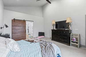 Bedroom with a barn door, ceiling fan, carpet, and high vaulted ceiling