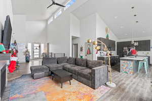 Living room with ceiling fan, light wood-type flooring, and high vaulted ceiling