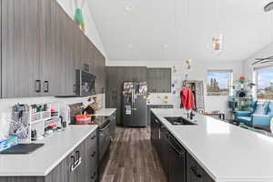 Kitchen with dark wood-type flooring, decorative light fixtures, stainless steel appliances, and a center island with sink