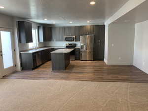 Kitchen with a kitchen island, appliances with stainless steel finishes, a textured ceiling, hardwood / wood-style flooring, and dark brown cabinetry