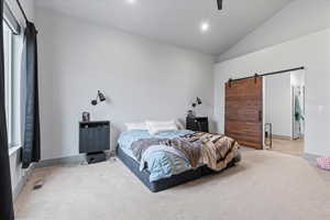 Bedroom with ceiling fan, a barn door, lofted ceiling, and light carpet