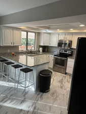 Kitchen featuring granite counters, a kitchen bar, kitchen peninsula, white cabinetry, and stainless steel appliances