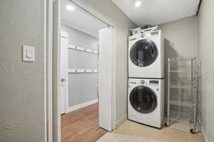 Laundry area with light hardwood / wood-style flooring and stacked washing maching and dryer