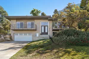 View of front of home featuring a mountain view, a front yard, a garage, and a balcony