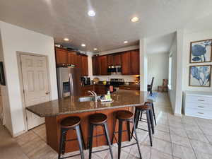 Kitchen with a textured ceiling, stainless steel appliances, a large island with sink, and a breakfast bar area