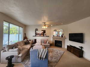 Living room featuring a tile fireplace, ceiling fan, light carpet, and a textured ceiling