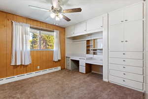 Bedroom with built in desk, wooden walls, light colored carpet, and ceiling fan