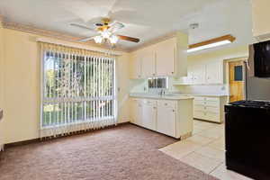 Kitchen/dining area featuring light carpet, travertine tile, kitchen peninsula,  cabinets, ceiling fan, and sink