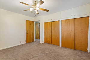 Another view of the Master Bedroom featuring two closets, light colored carpet, and ceiling fan