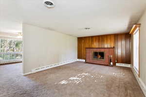 Living room featuring a baseboard radiator, wooden walls, a fireplace, and carpet