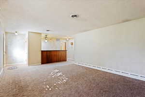 Another view of the living room a baseboard radiator, a textured ceiling, and carpet floors