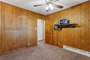 Bedroom featuring a baseboard heating unit, ceiling fan, light colored carpet, and wood walls