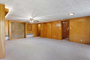 Interior space with radiator, light carpet, wood walls, and ceiling fan