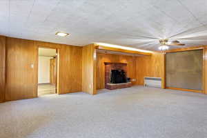 Another view of living room with wood walls, radiator heating unit, carpet, and ceiling fan