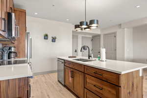 Kitchen with a sink, stainless steel appliances, brown cabinetry, light wood-type flooring, and baseboards