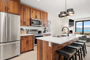 Kitchen with stainless steel appliances, brown cabinets, light countertops, open floor plan, and a kitchen breakfast bar
