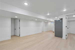 Basement featuring stainless steel fridge, a textured ceiling, and light wood-type flooring