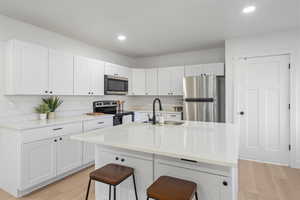 Kitchen featuring sink, a breakfast bar, white cabinets, light wood-type flooring, and appliances with stainless steel finishes