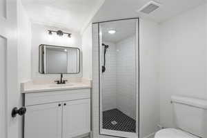 Bathroom with vanity, toilet, a textured ceiling, and tiled shower