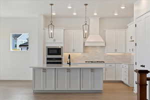 Kitchen featuring appliances with stainless steel finishes, hanging light fixtures, white cabinetry, and an island with sink