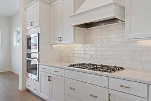 Kitchen featuring stainless steel appliances, light stone countertops, light wood-type flooring, white cabinetry, and premium range hood