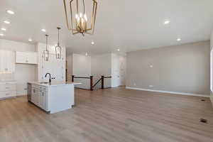 Kitchen featuring light hardwood / wood-style flooring, white cabinetry, pendant lighting, and an island with sink