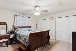 Bedroom featuring two closets, light colored carpet, and ceiling fan