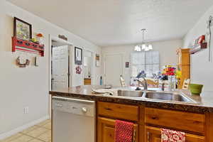 Kitchen featuring a textured ceiling, a chandelier, dishwasher, light tile patterned flooring, and sink