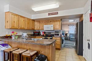 Kitchen featuring kitchen peninsula, light tile patterned floors, appliances with stainless steel finishes, a breakfast bar area, and sink