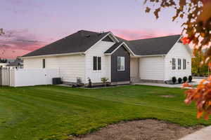 Back house at dusk with a lawn and cooling unit