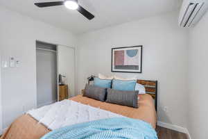 Bedroom featuring a closet with sliding mirror doors, ceiling fan, wood-type flooring, and a wall mounted mini split heating and cooling unit