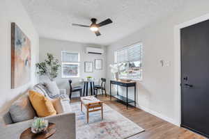 Living room featuring an wall mounted mini split heating and cooling unit, hardwood / wood-style flooring, ceiling fan, and a wealth of natural light