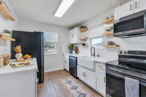 Kitchen featuring white cabinetry, open shelving, black stainless steel appliances, light wood-type flooring, and tasteful backsplash