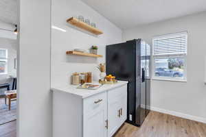 Kitchen with white cabinetry, light hardwood / wood-style flooring, open shelving, and black stainless fridge with ice dispenser